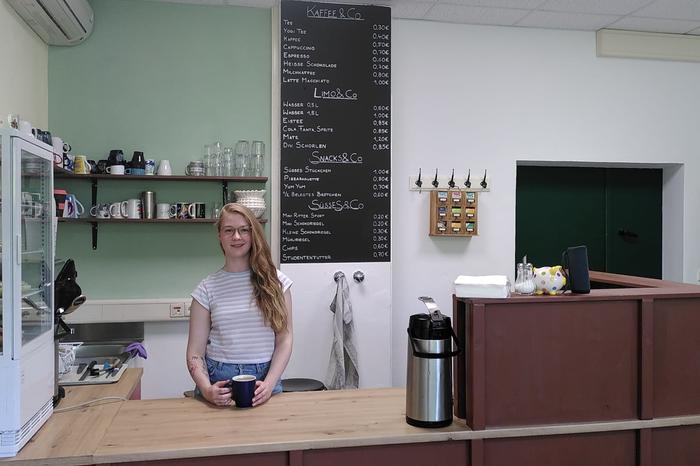 Person standing behind cafe bar with menu and shelves in the background