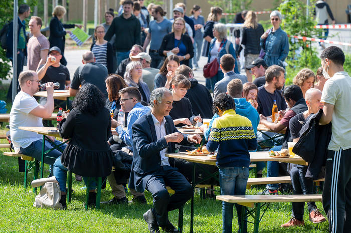 People sitting outside in the sun around tables having food and drinks